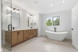 Contemporary bathroom featuring a freestanding tub, a dual vanity with wood-finish cabinetry, a glass-enclosed shower, and light-toned tile flooring - 