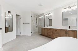 Spacious bathroom featuring a dual vanity with wood-finish cabinetry and quartz countertops, a large frameless glass shower enclosure, and light-toned tile flooring - 