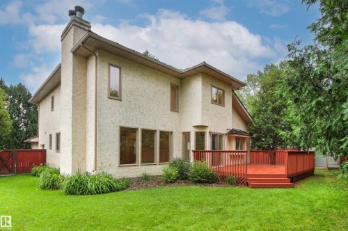 Rear exterior featuring a large red-stained wood deck with stairs, a stucco finish, multiple windows, and a prominent chimney - 140 Healy Road Nw, Edmonton, AB - Outdoor