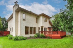 Rear exterior featuring a large red-stained wood deck with stairs, a stucco finish, multiple windows, and a prominent chimney - 