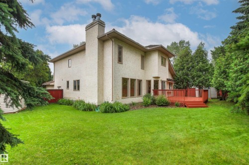 Spacious rear yard featuring a large red-stained wood deck, stucco exterior, mature trees, a prominent chimney, and multiple windows - 140 Healy Road Nw, Edmonton, AB - Outdoor
