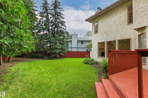 Expansive green lawn framed by mature trees, featuring a red-stained wooden deck with steps and a privacy fence - 140 Healy Road Nw, Edmonton, AB - Outdoor