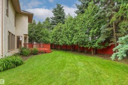 Expansive rear yard featuring a vibrant red-stained deck with railing, a lush green lawn, mature trees providing natural screening, a red privacy fence, and a stucco exterior with multiple windows - 