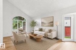 Vaulted ceiling living space featuring an arched picture window, wood-finish flooring, and crisp white walls - 