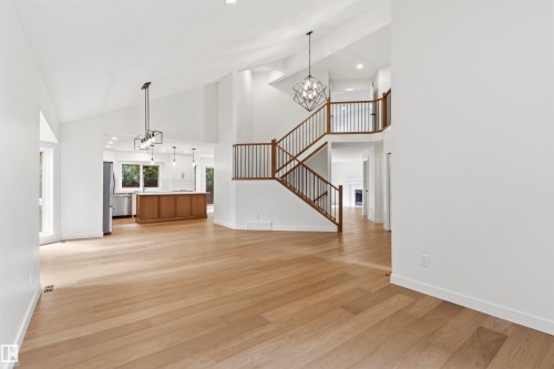 Spacious interior featuring soaring vaulted ceilings, light wood-finish flooring, a contemporary staircase with dark wood railings, a kitchen with a wood-toned island, and modern pendant lighting - 140 Healy Road Nw, Edmonton, AB - Indoor Photo Showing Other Room
