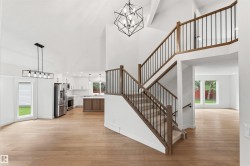 Bright interior featuring high ceilings, wood-finish flooring, a contemporary staircase with iron balusters, a kitchen with stainless steel appliances, and large windows - 