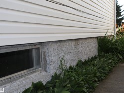 White vinyl siding exterior with a rectangular basement window featuring a metal frame - 