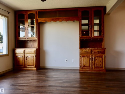 Built-in cabinetry with glass-front uppers and lower storage, featuring wood-finish flooring and natural light from a nearby window - 4306 - 55 Ave, Barrhead, AB - Indoor Photo Showing Other Room
