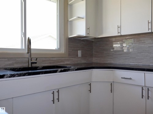 White cabinetry featuring sleek hardware, black countertops, undermount sink, and a tiled backsplash - 4306 - 55 Ave, Barrhead, AB - Indoor Photo Showing Kitchen With Double Sink
