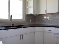 White cabinetry featuring sleek hardware, black countertops, undermount sink, and a tiled backsplash - 