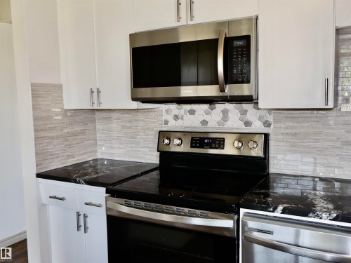 Modern kitchen featuring white cabinetry, black countertops, stainless steel appliances, and a tiled backsplash - 4306 - 55 Ave, Barrhead, AB - Indoor Photo Showing Kitchen With Upgraded Kitchen