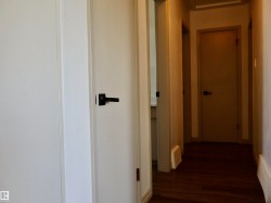 Hallway featuring wood-finish flooring, white paneled doors, and matte black door hardware - 