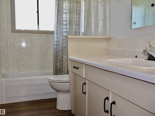 Bathroom featuring wood-finish flooring, a white vanity with black hardware, an integrated sink, a built-in bathtub, and a tiled shower surround - 4306 - 55 Ave, Barrhead, AB - Indoor Photo Showing Bathroom