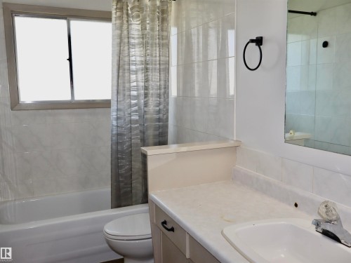 Bathroom featuring a built-in bathtub, a window, wall-mounted tiling, a vanity with an integrated sink, and a wall mirror - 4306 - 55 Ave, Barrhead, AB - Indoor Photo Showing Bathroom
