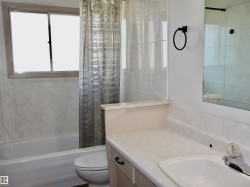Bathroom featuring a built-in bathtub, a window, wall-mounted tiling, a vanity with an integrated sink, and a wall mirror - 
