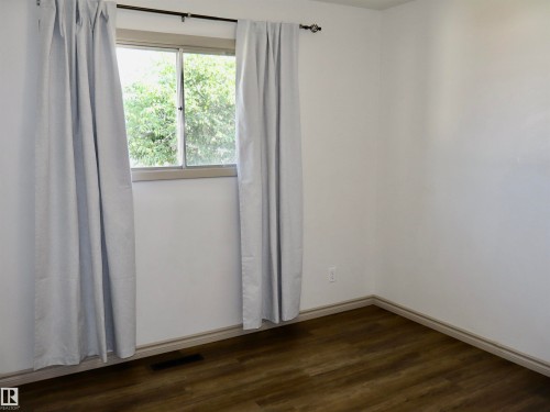 Interior room featuring wood-finish flooring, white walls, and a window with light-colored curtains on a dark curtain rod - 4306 - 55 Ave, Barrhead, AB - Indoor Photo Showing Other Room