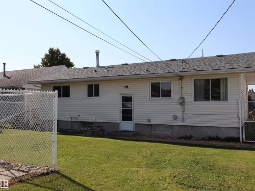 Rear exterior featuring beige horizontal siding, a gray shingle roof, a chain-link fence, and a green lawn - 4306 - 55 Ave, Barrhead, AB - Outdoor With Exterior