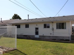 Rear exterior featuring beige horizontal siding, a gray shingle roof, a chain-link fence, and a green lawn - 