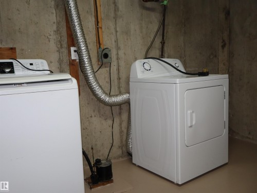 Dedicated laundry area featuring a white washing machine, white dryer, concrete wall, wood accents, and a utility pump - 4306 - 55 Ave, Barrhead, AB - Indoor Photo Showing Laundry Room