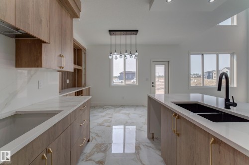 Open-concept kitchen featuring wood-finish cabinetry, light-toned countertops, and a central island with an undermount double sink and matte black faucet - 4723 17 Avenue Sw, Edmonton, AB - Indoor Photo Showing Kitchen With Double Sink