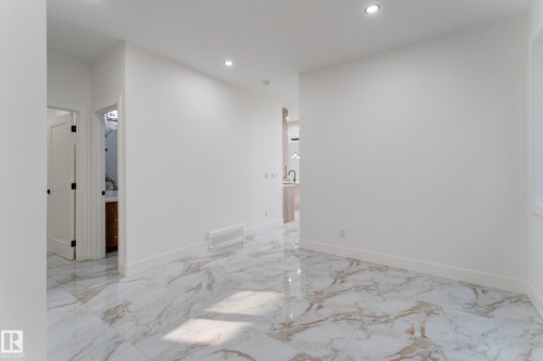 Spacious room featuring large format marble-look tile flooring, white baseboards, recessed ceiling lighting, and a white interior door with dark hardware - 4723 17 Avenue Sw, Edmonton, AB - Indoor Photo Showing Other Room