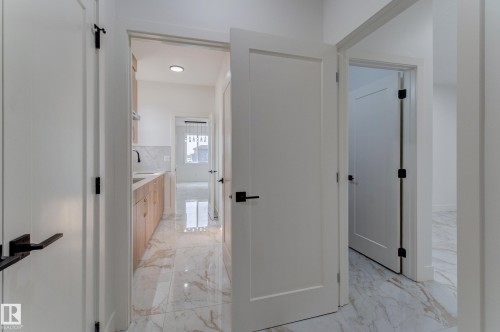 Hallway entry featuring white paneled doors with matte black hardware, leading to a utility space with wood-finish cabinetry, a white countertop, a black faucet, and a white tile backsplash - 4723 17 Avenue Sw, Edmonton, AB - Indoor Photo Showing Other Room