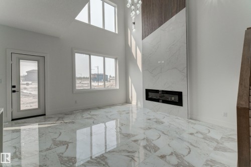 Great room featuring a contemporary electric fireplace with a floor-to-ceiling marble-look surround, a wood-slat accent wall, and a multi-tiered chandelier - 4723 17 Avenue Sw, Edmonton, AB - Indoor With Fireplace