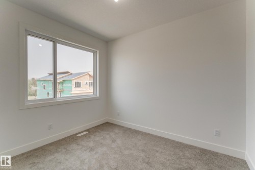 Bright room featuring a large window, plush gray carpet, white walls, and clean white baseboards - 4723 17 Avenue Sw, Edmonton, AB - Indoor Photo Showing Other Room