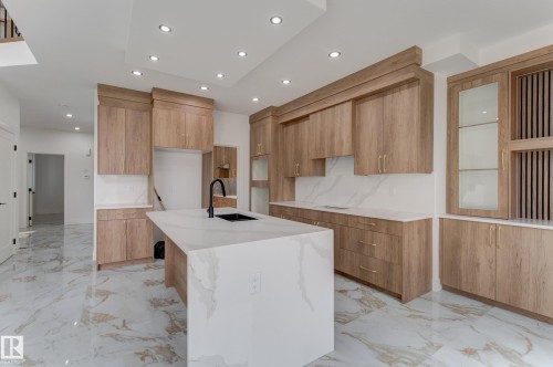 Modern kitchen featuring a waterfall island with a matte black faucet, light wood-finish cabinetry, white marble-look countertops and backsplash, recessed lighting, and large format marble-look floor tiles - 4723 17 Avenue Sw, Edmonton, AB - Indoor Photo Showing Kitchen