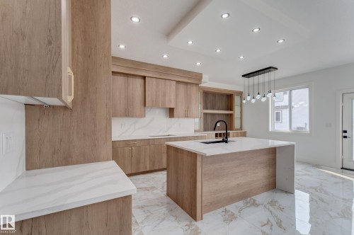 Modern kitchen featuring wood-finish cabinetry, white countertops, and a central island with an integrated sink - 4723 17 Avenue Sw, Edmonton, AB - Indoor Photo Showing Kitchen