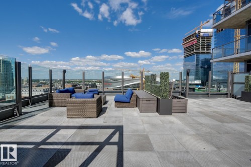 Expansive rooftop patio featuring large format paver flooring, glass panel railings, and artificial hedge planters - #910 10238 103 St Nw, Edmonton, AB - Outdoor