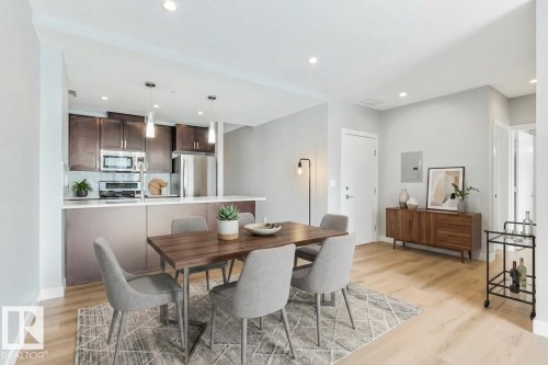 Open-concept living space featuring wood-finish flooring, a kitchen with dark wood cabinetry, stainless steel appliances, and a breakfast bar with pendant lighting - #910 10238 103 St Nw, Edmonton, AB - Indoor Photo Showing Dining Room