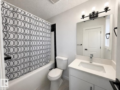 Bathroom featuring a white vanity with an integrated sink and light-toned countertop, a frameless mirror, and a three-light vanity fixture - 3799 21 Street Nw, Edmonton, AB - Indoor Photo Showing Bathroom