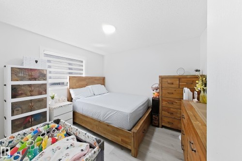 Bright interior space featuring light wood-finish flooring, a window with horizontal blinds, and a built-in overhead light fixture - 3799 21 Street Nw, Edmonton, AB - Indoor Photo Showing Bedroom