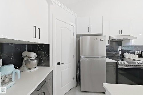 Modern kitchen featuring white upper cabinetry, dark lower cabinetry, and contrasting black marble-look backsplash - 3799 21 Street Nw, Edmonton, AB - Indoor Photo Showing Kitchen