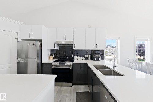 Modern kitchen featuring dual-toned cabinetry with white upper and dark lower units, a sleek black marble-look backsplash, stainless steel appliances, and a double basin undermount sink - 3799 21 Street Nw, Edmonton, AB - Indoor Photo Showing Kitchen With Double Sink With Upgraded Kitchen