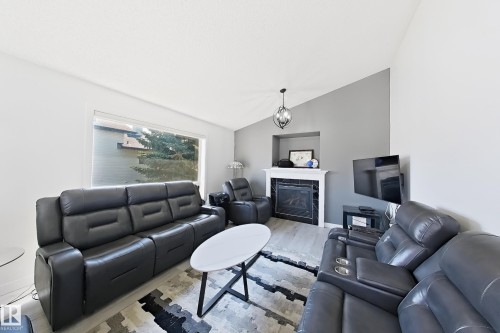 Spacious living area featuring a vaulted ceiling and a prominent fireplace with a white mantel and dark surround - 3799 21 Street Nw, Edmonton, AB - Indoor Photo Showing Living Room With Fireplace