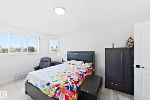 Bright bedroom featuring multiple windows, light wood-finish flooring, a contemporary ceiling light fixture, and a white paneled door with matte black hardware - 3799 21 Street Nw, Edmonton, AB - Indoor Photo Showing Bedroom