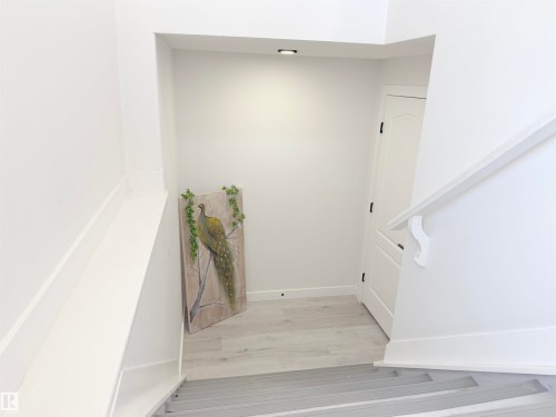 Stairwell featuring light wood-finish flooring, white painted walls, a white handrail with decorative brackets, a white paneled door with black hardware, and recessed ceiling lighting - 3799 21 Street Nw, Edmonton, AB - Indoor Photo Showing Other Room
