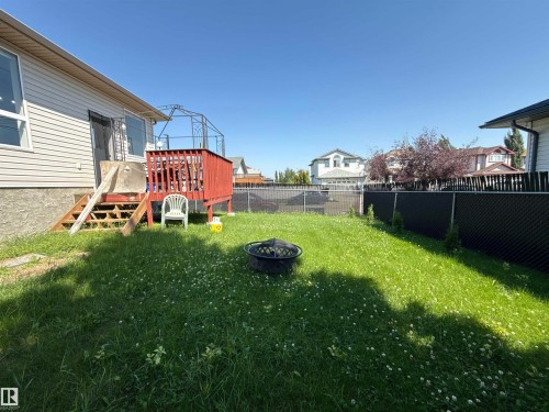 Expansive backyard featuring a wood deck with red railings, a chain-link fence with privacy slats, and a fire pit - 3799 21 Street Nw, Edmonton, AB - Outdoor