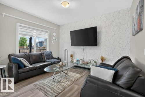 Living area featuring wood-finish flooring, a large window with roller shades, and a feature wall with patterned wallpaper - 848 Ebbers Crescent Nw, Edmonton, AB - Indoor Photo Showing Living Room