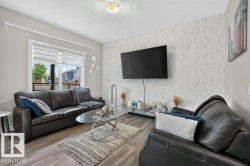 Living area featuring wood-finish flooring, a large window with roller shades, and a feature wall with patterned wallpaper - 