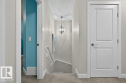 Carpeted hallway featuring a contemporary pendant light fixture, white interior doors with brushed nickel hardware, and a white handrail leading to a lower level - 