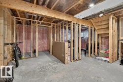 Unfinished basement featuring wood framing, concrete flooring, exposed ceiling joists, and a visible staircase - 