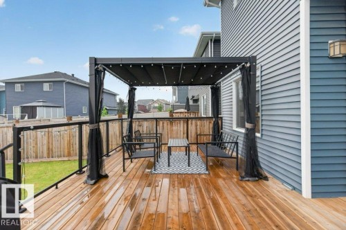 Spacious wood-finish deck featuring a black metal pergola with a retractable canopy, string lighting, and glass panel railings - 848 Ebbers Crescent Nw, Edmonton, AB - Outdoor With Deck Patio Veranda With Exterior