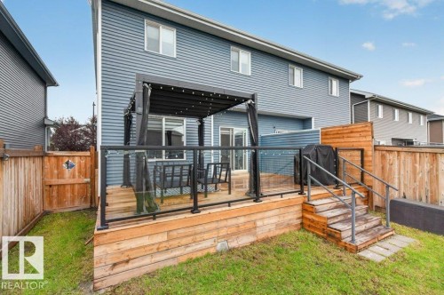 Expansive wooden deck featuring glass panel railings, a black metal pergola with string lights, and exterior stairs with metal handrails - 848 Ebbers Crescent Nw, Edmonton, AB - Outdoor With Deck Patio Veranda With Exterior