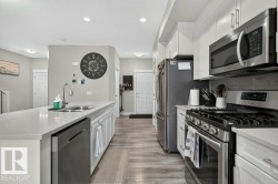 Modern kitchen featuring an expansive island with an undermount sink, stainless steel appliances, white shaker-style cabinetry, light wood-finish flooring, and recessed lighting - 