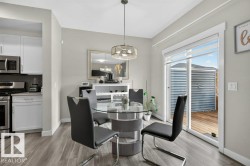 Open-concept dining area featuring wood-finish flooring, a contemporary pendant light fixture, and a sliding glass door providing access to an exterior deck - 
