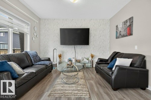 Living area featuring wood-finish flooring, a patterned accent wall, and large windows - 848 Ebbers Crescent Nw, Edmonton, AB - Indoor Photo Showing Living Room
