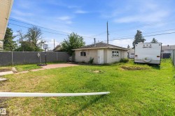 Expansive grassy yard area featuring a paved patio and an outbuilding with two windows - 